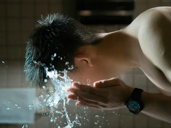 洗面台で水を顔にすくって洗う男性